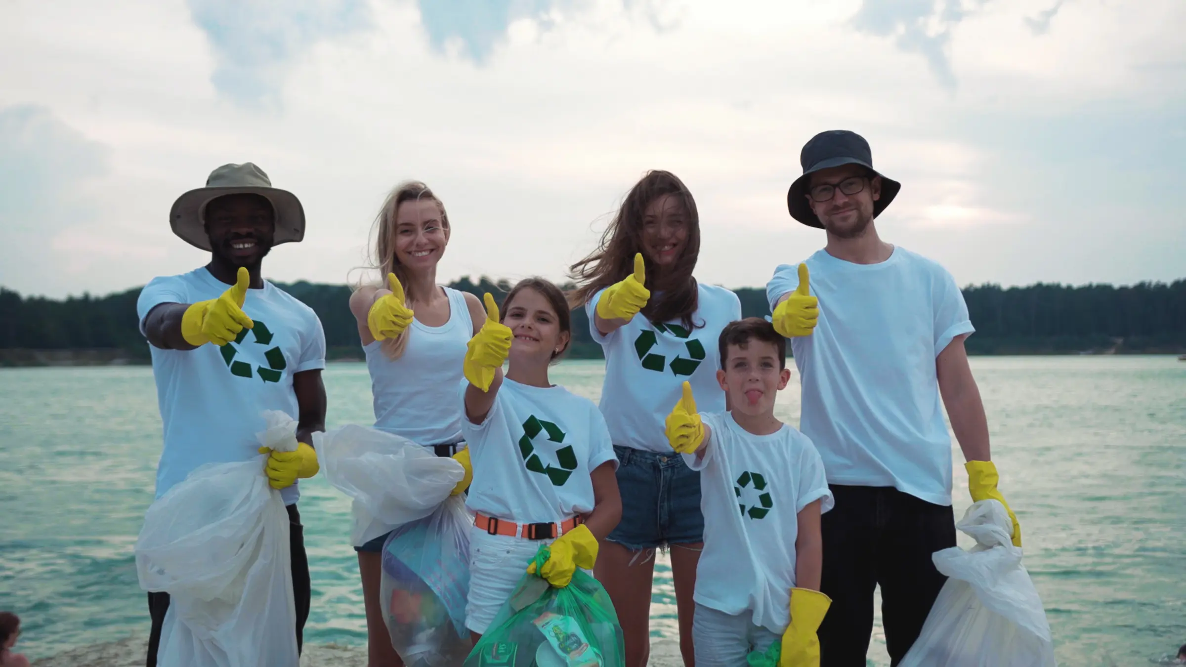 A group of volunteers in recycling shirts holding collection bags at a shoreline cleanup