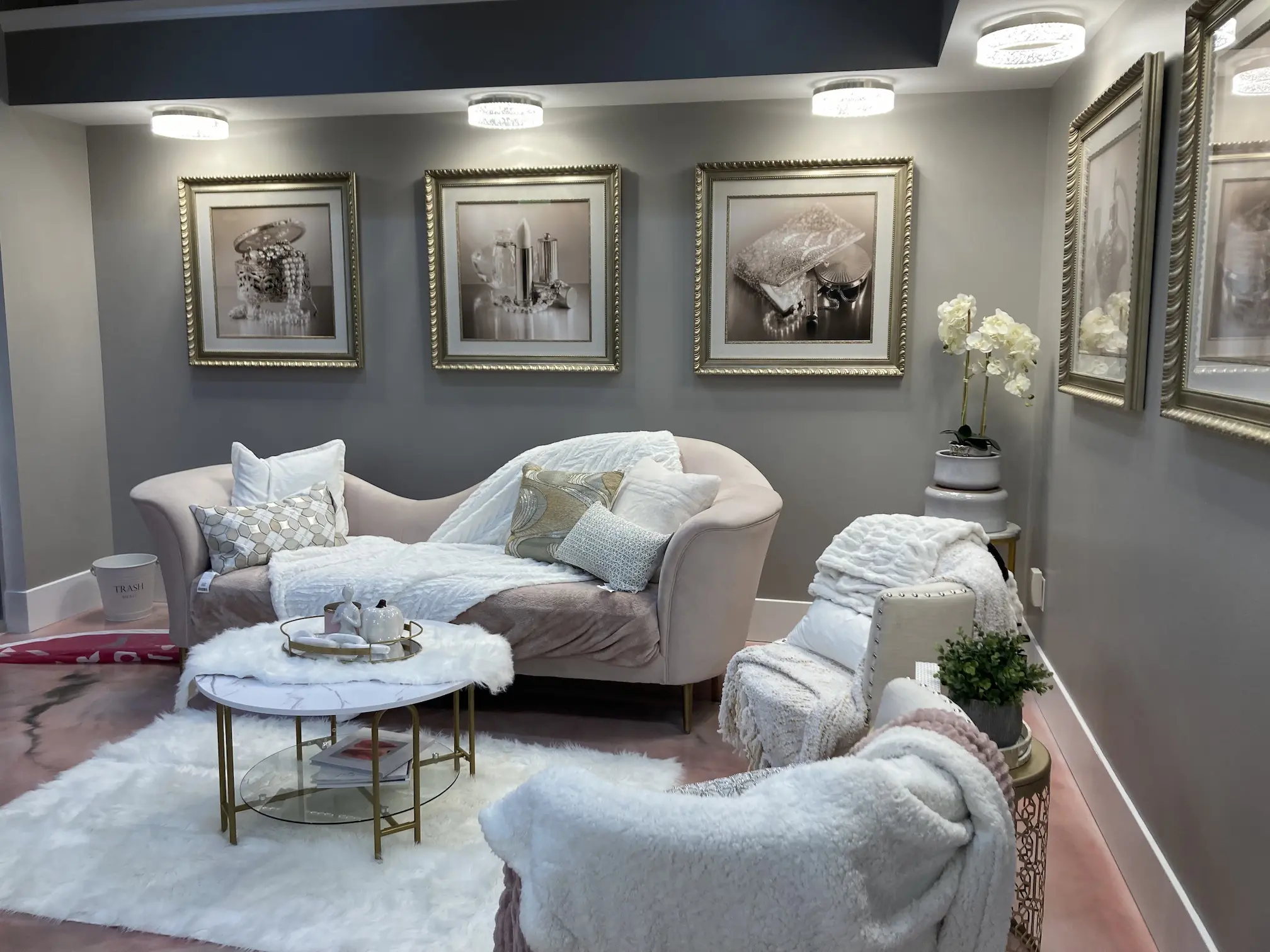Reception area of an Iowa salon built by Team 218, with a blush chaise, framed prints, and white orchids